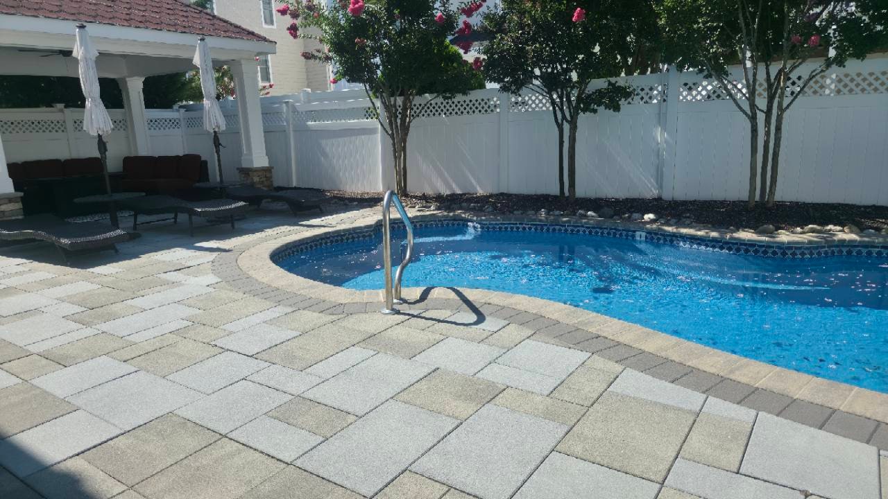 Clean paver pool surround with flowering trees and a shaded pavilion